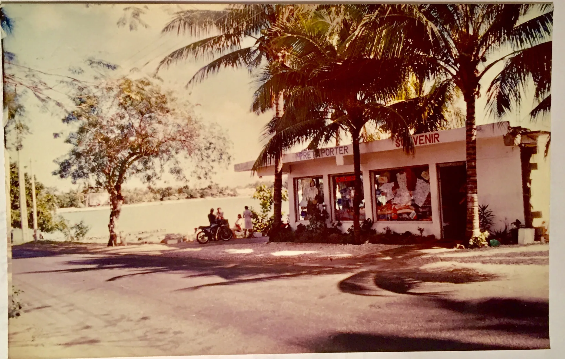 La boutique « Souvenir de Grand Baie » à Grand Baie, 1985 — ses enseignes Prêt à Porter et Souvenir sous les cocotiers, une moto garée devant